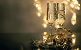 close up of two flute glasses filled with sparkling wine wuth ribbons and christmas decor